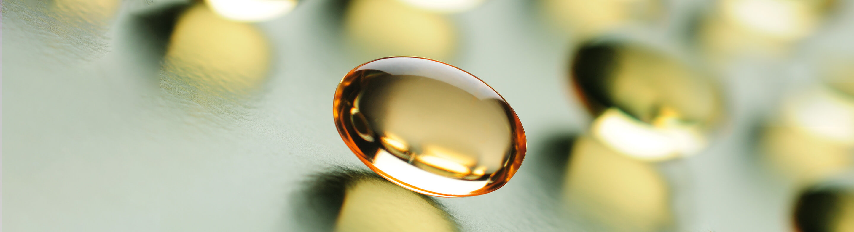 Cápsula de aceite omega 3 dorada y traslúcida sobre fondo difuminado. Nutriente esencial para la hidratación y regeneración de la salud de la piel.